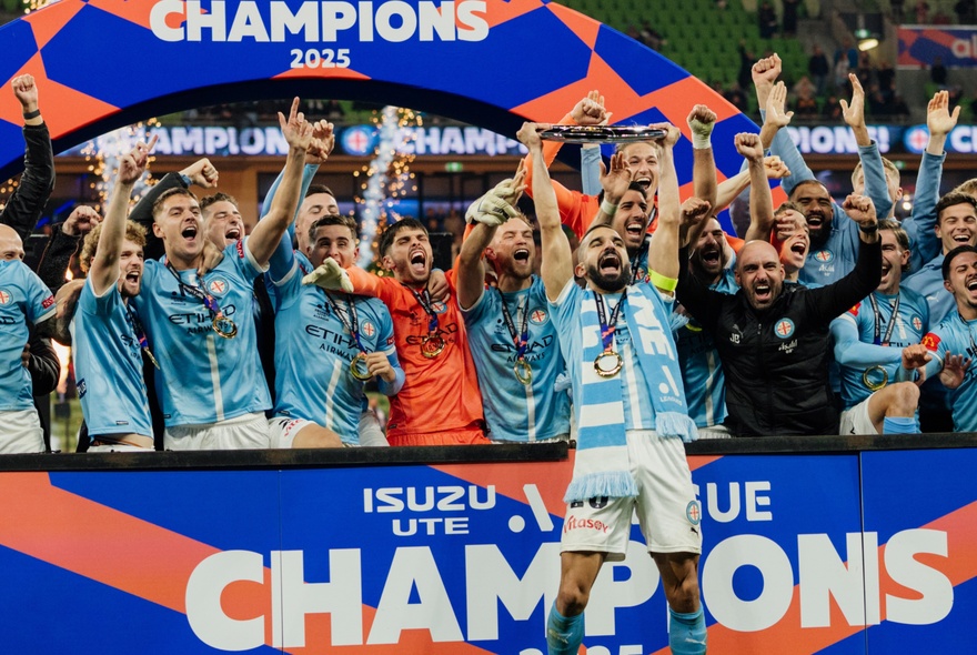 A mens soccer team in pale blue kit raising arms in celebration.