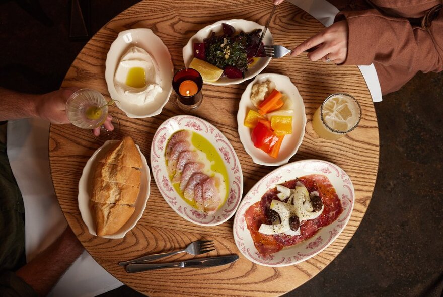 Two people at a wooden dining table enjoying a selection of dishes.