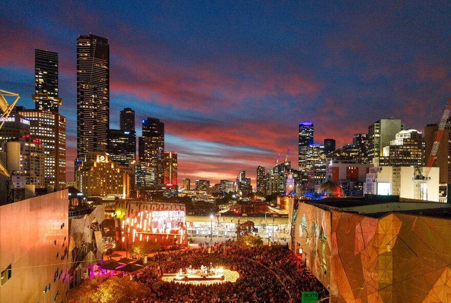 A candlelight concert taking place in the main plaza at Fed Square, the Melbourne city building skyline in the background.