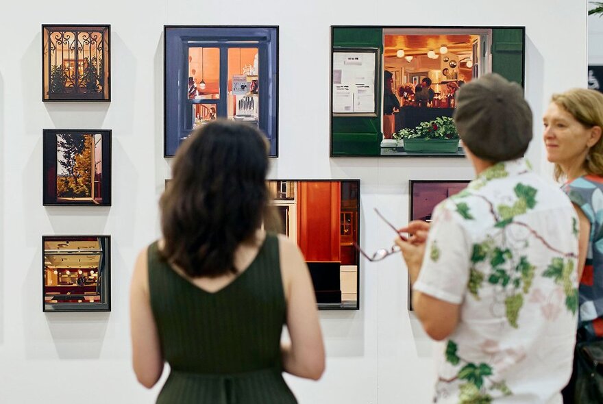 People standing in front of several artworks hung close together on an art gallery wall.