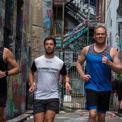 Three men in singlets and shorts running down a laneway with the walls covered in street art.