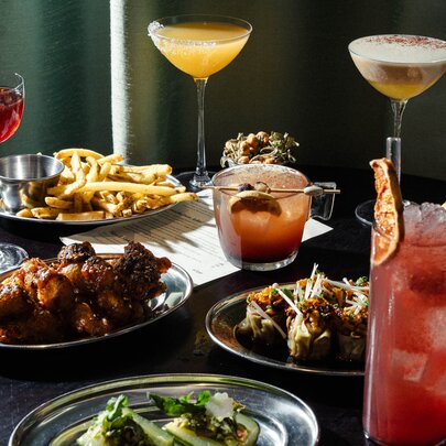 A table with multiple cocktails, next to plates of bar snacks served in small metal bowls.