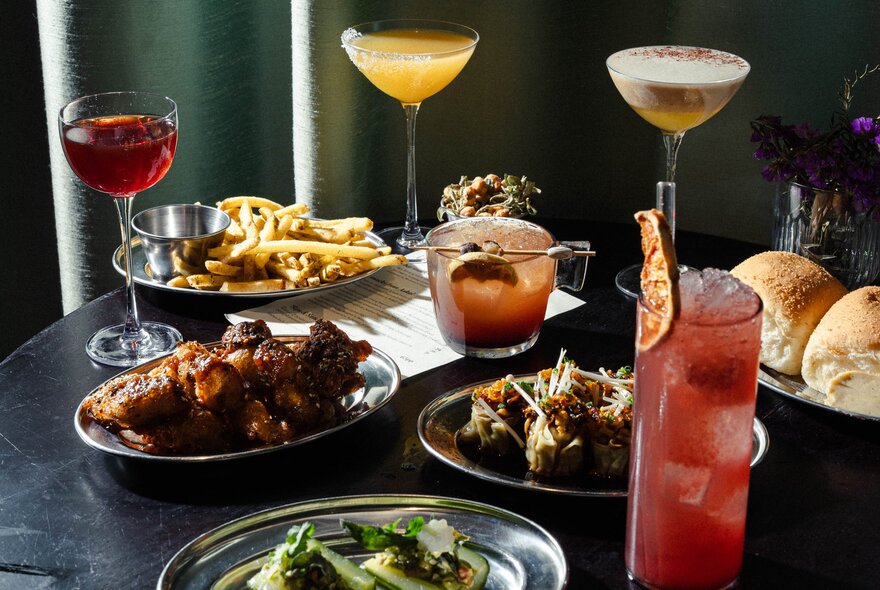 A table with multiple cocktails, next to plates of bar snacks served in small metal bowls.