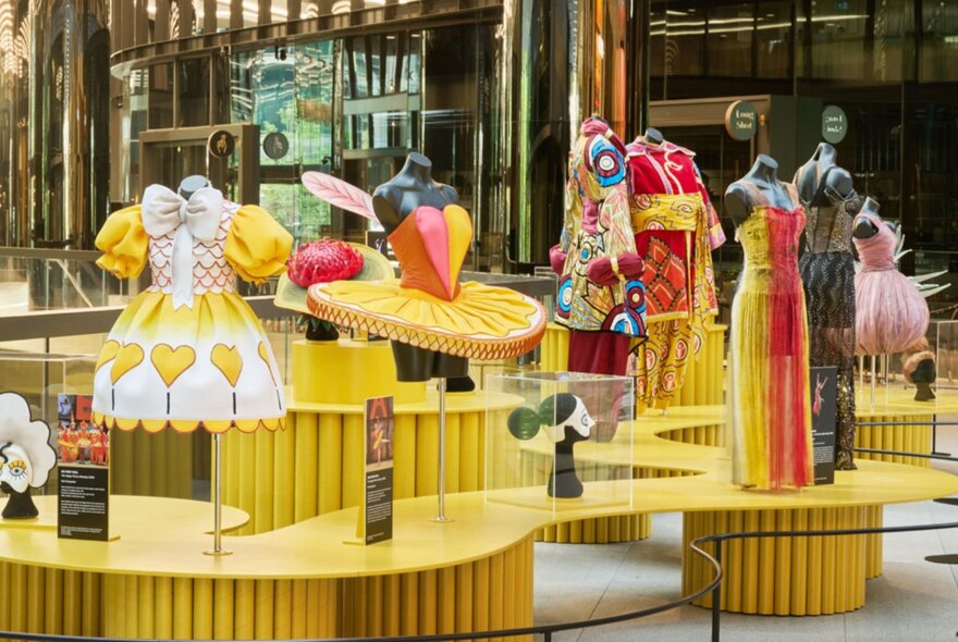 A fashion exhibit with numerous outfits on yellow stands. 