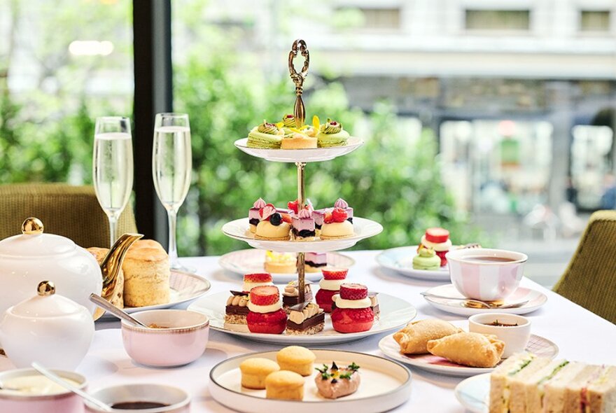 A table set for high tea with champagne glasses and a three-tiered cake tray, as well as a teapot and teacups. 