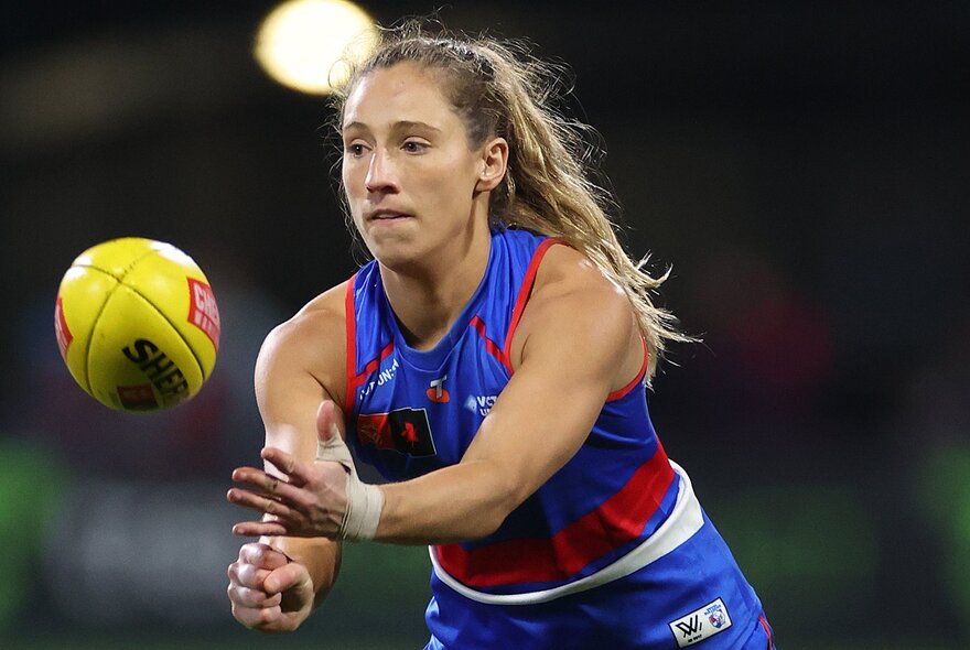 A Western Bulldogs AFLW player handballing a yellow Sherrin football.