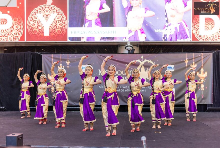 Diwali dancers in gold and purple costumes performance a dance on stage at Marvel Stadium.