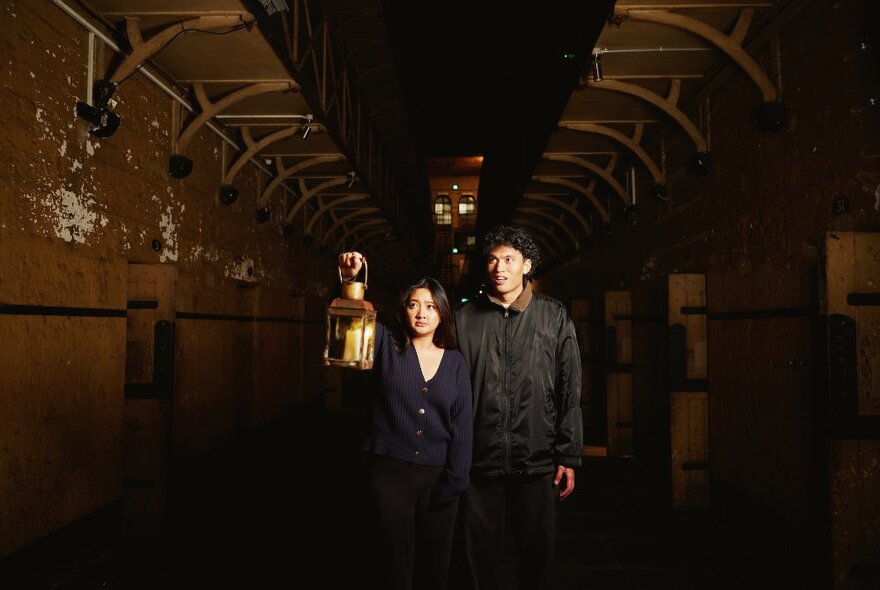 Two people in Old Melbourne Gaol walking along a darkend