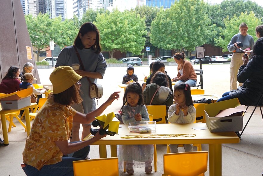 Family groups participating in art and craft activities at low tables in the outdoor area at ACCA gallery.