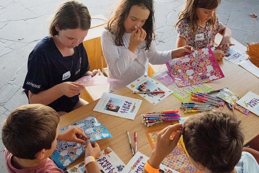 Children seated around a table with pencils and craft booklets.