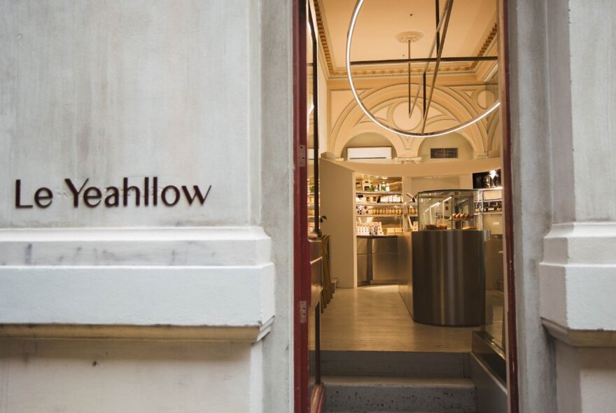 The exterior of the cafe and cake shop Le Yeahllow, with signage on the concrete wall, and an open doorway leading into an inviting interior.