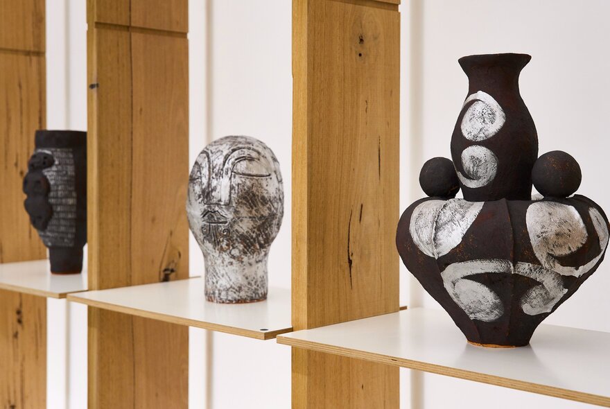Three black and white contemporary ceramics on display on a shelf in a gallery.