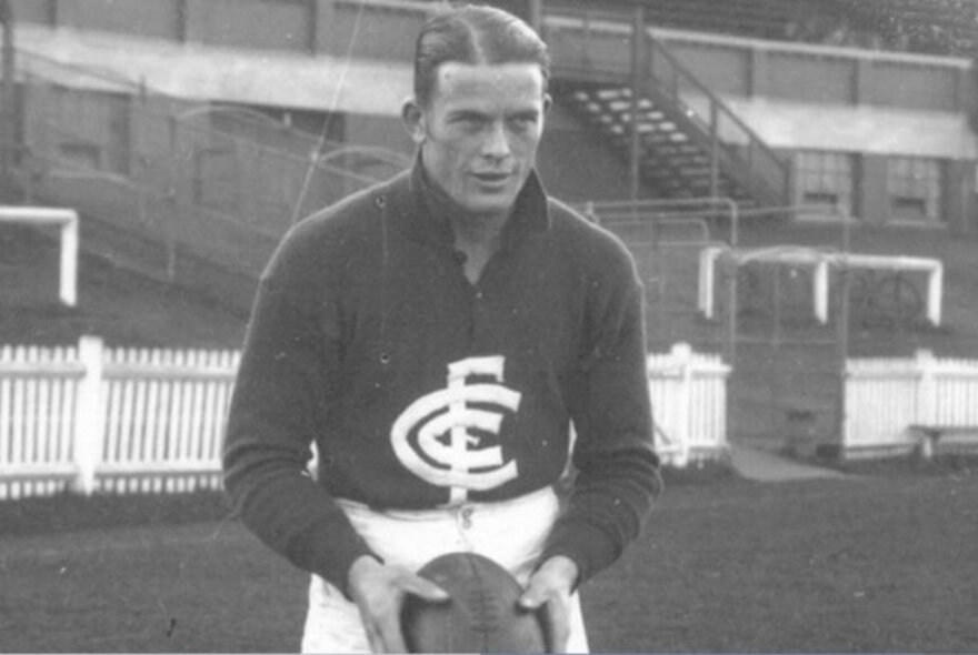A black and white photograph from 1945 of a football player wearing a Carlton Football Club jersey and white shorts, holding a football.