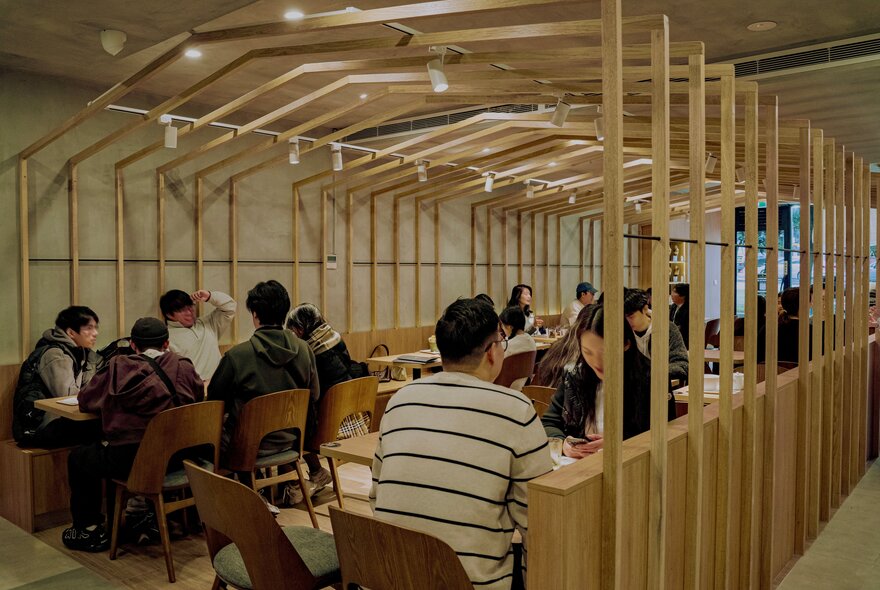 A group of people sat around tables under a wooden beam structure in a cafe.