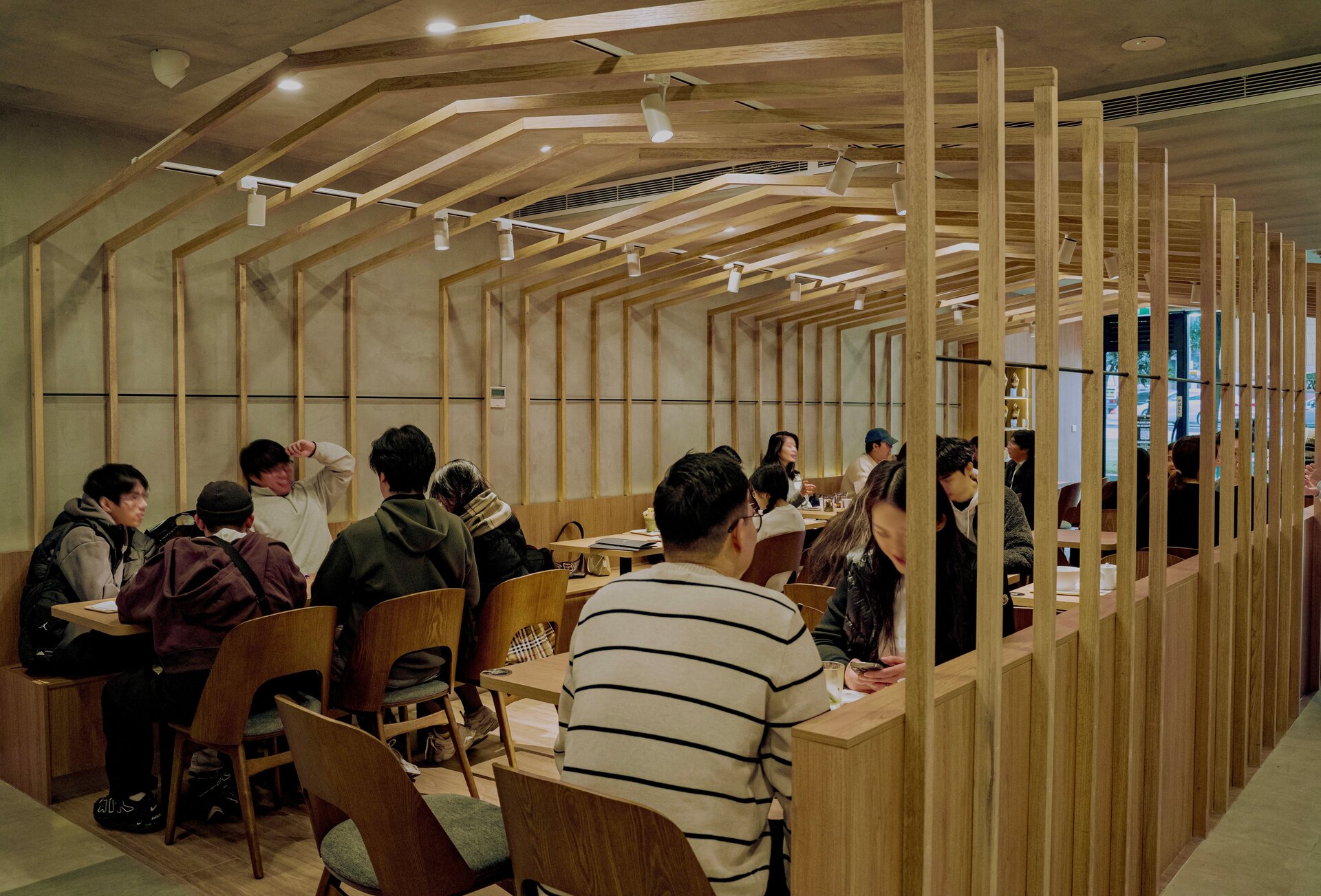 A group of people sat around tables under a wooden beam structure in a cafe.