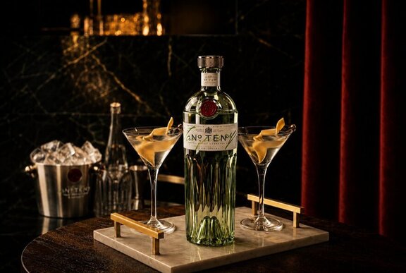 Two martini cocktails on a tray with a bottle of gin, set against a red velvet curtain.