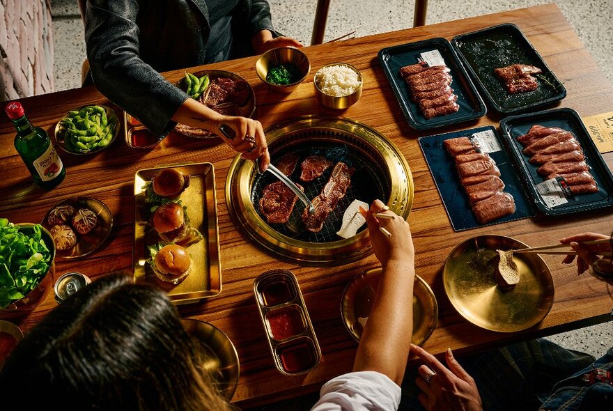 Diners seated at a table BBQ with a central grill and platters of meat.