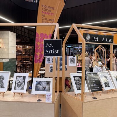 A stall at a craft market displaying pet portraits.