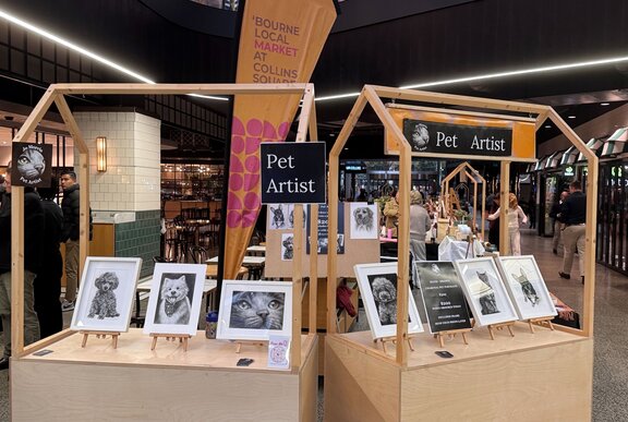 A stall at a craft market displaying pet portraits.