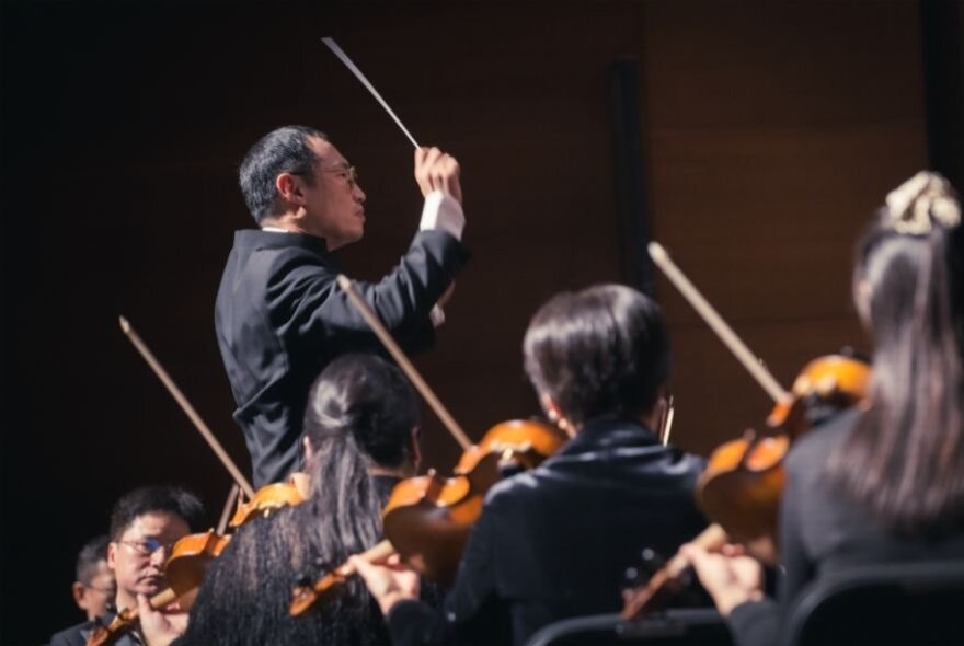 Conductor leading an orchestra of violinists.