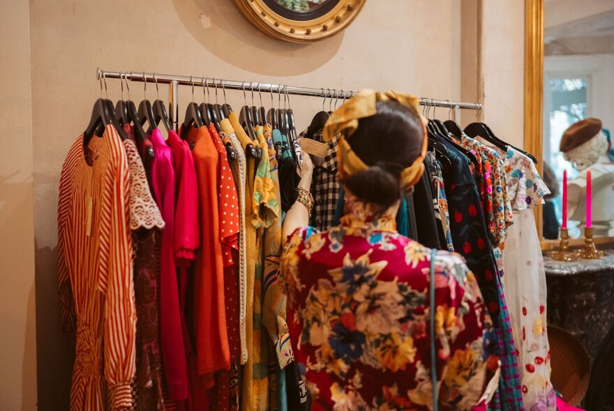 The back of a woman with a patterned robe looking at a rack of coloured clothing. 