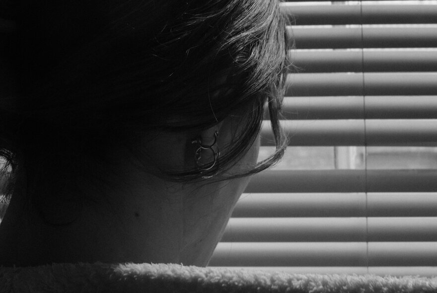 A person's face in silhouette against broken venetian blinds.