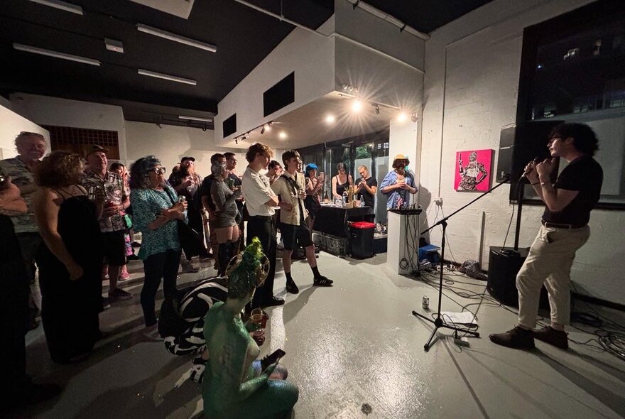 Person performing at a mike stand in a studio space with people looking on.