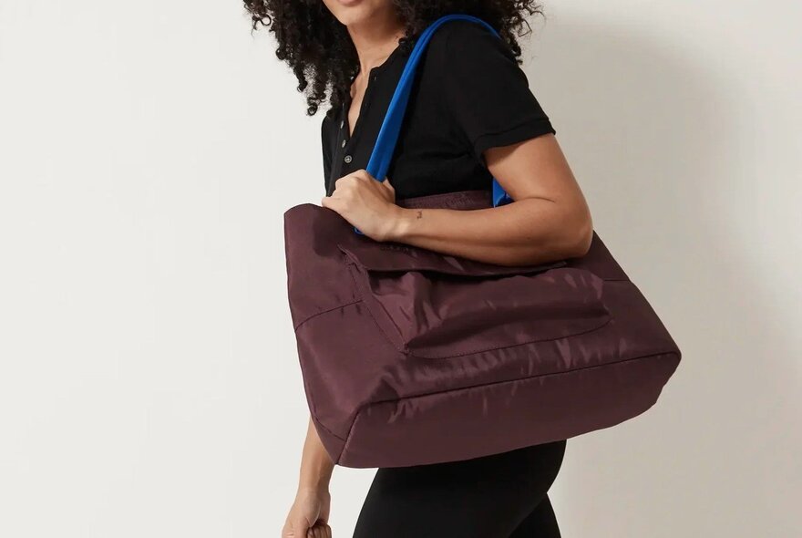 A woman is holding a large purple tote with a blue strap