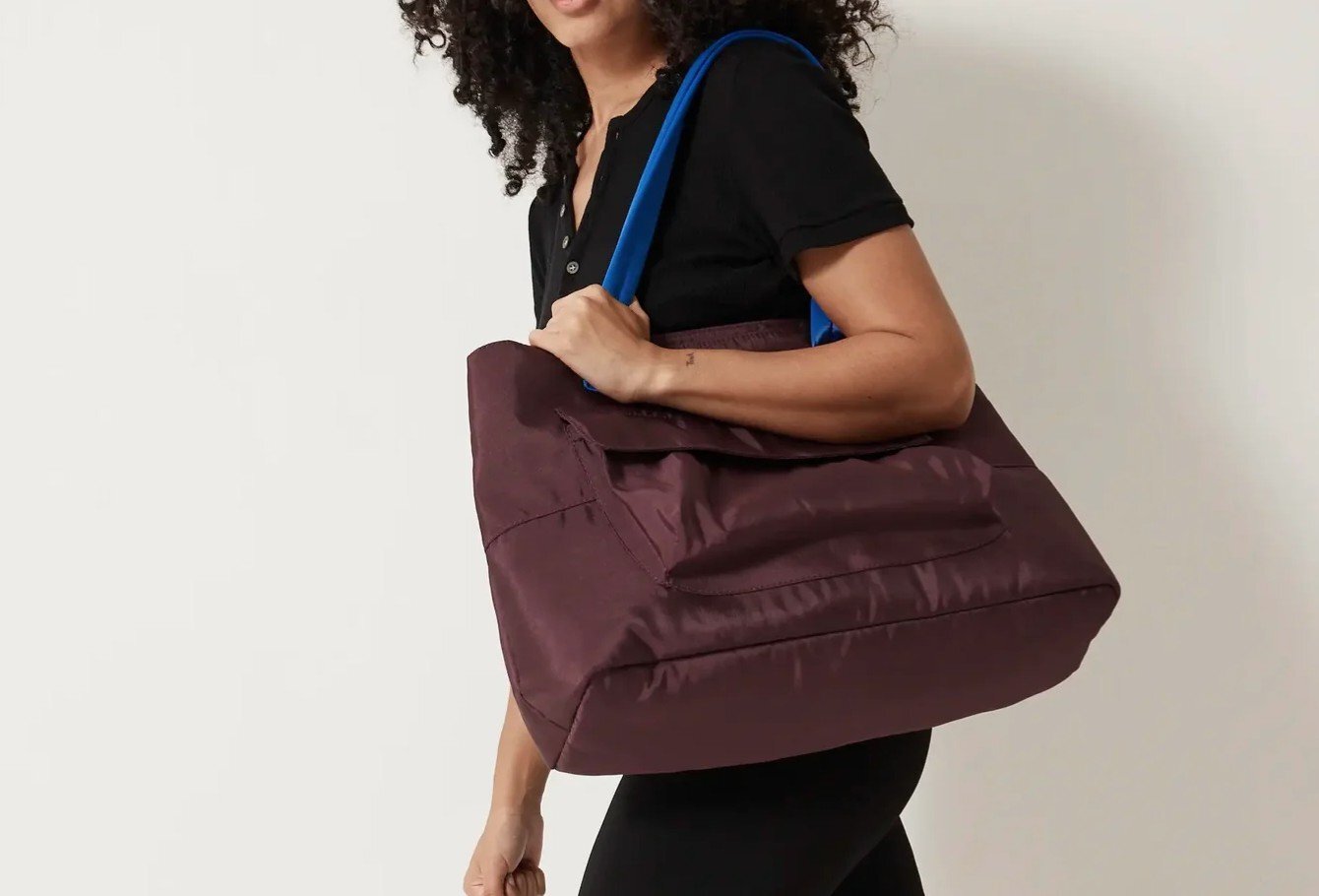 A woman is holding a large purple tote with a blue strap