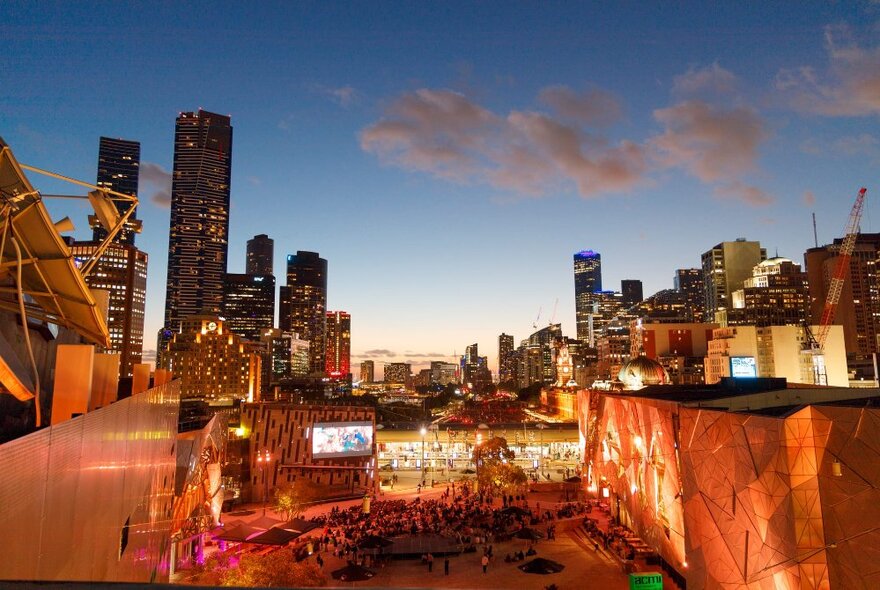 The Melbourne city skyline seen from behind Fed Square at dusk.