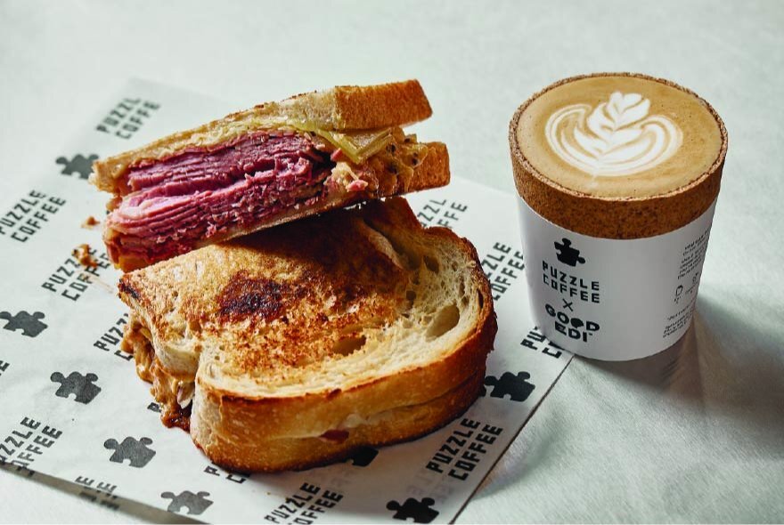 A sliced toasted sandwich and a takeaway coffee cup resting on a marble table-top.