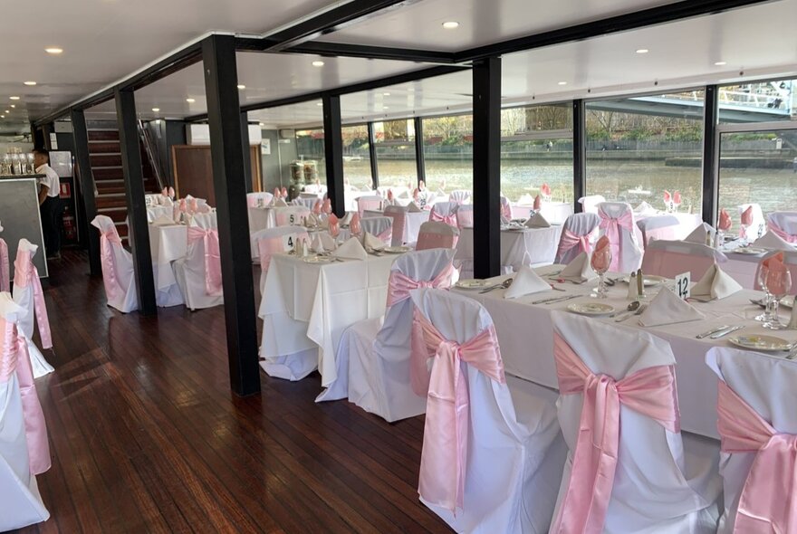 The interior of a harbour cruise restaurant vessel with white tablecloths and chair coverings with pink satin bows.