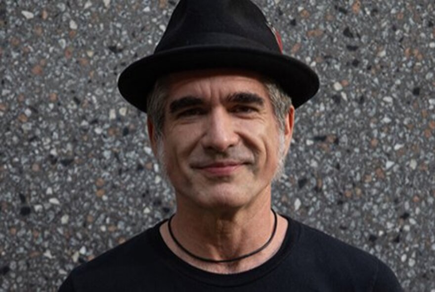 Singer Jack Jones smiling and wearing a black t-shirt and black pork pie hat.