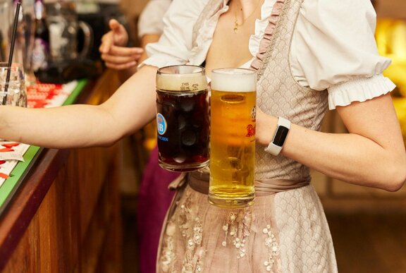 A waitress holding two beers wearing a dirndl.