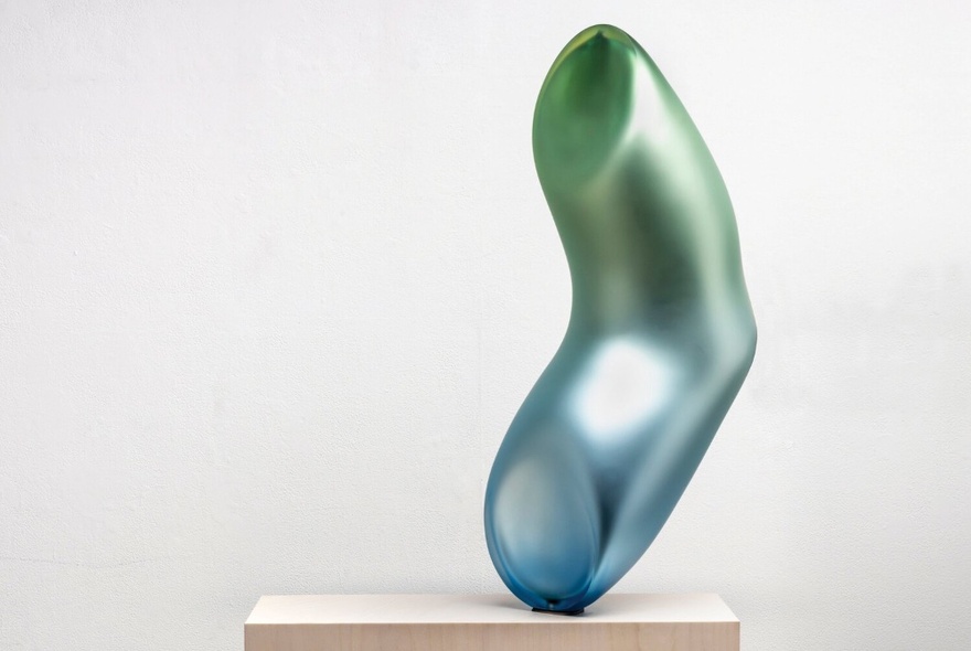 A shiny metal, organically shaped, tubular blue and green sculpture on a plinth.