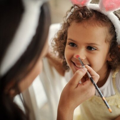 Young girl wearing rabbit ears, having her face painted.