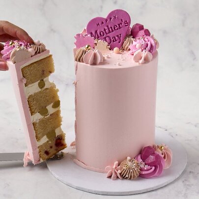 A pink cake decorated for Mother's Day with a slice being cut out.