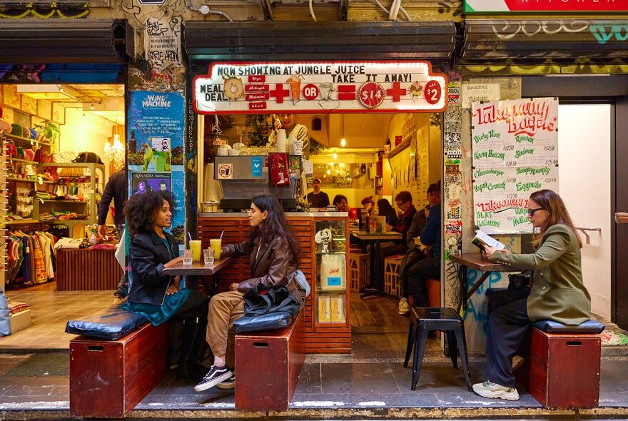 Three people dining on benches outside a tiny laneway cafe.