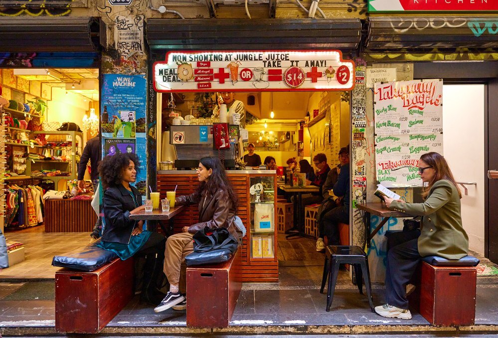 Three people dining on benches outside a tiny laneway cafe.