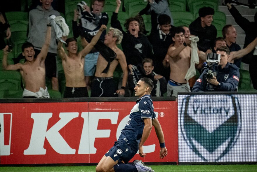 A soccer player on his knees in front of fans in the stands.