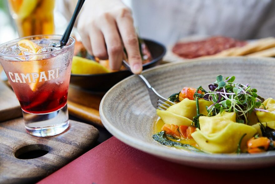 Hand pushing fork into grey bowl with gnocchi and herbs atop.