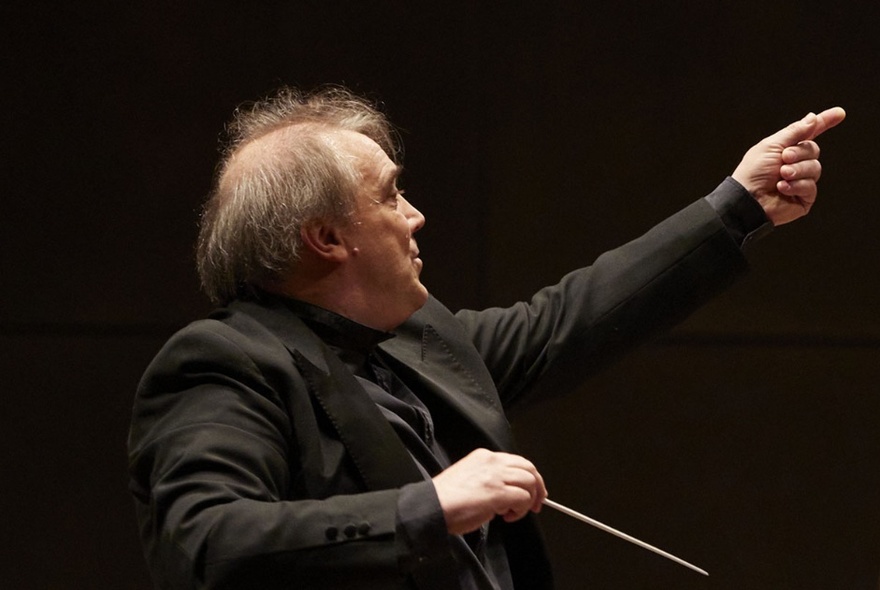 Older conductor with balding grey hair, holding a baton.