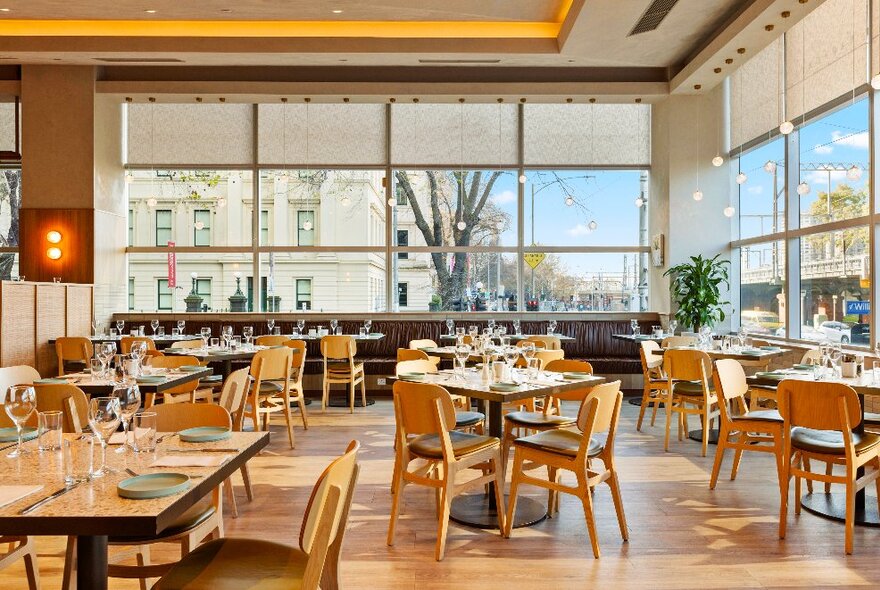 Light and airy hotel dining area with large windows looking onto city streets, wooden tables and chairs.