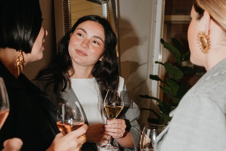 Three women enjoying a glass of wine and a chat, two looking away from the camera and one smiling.