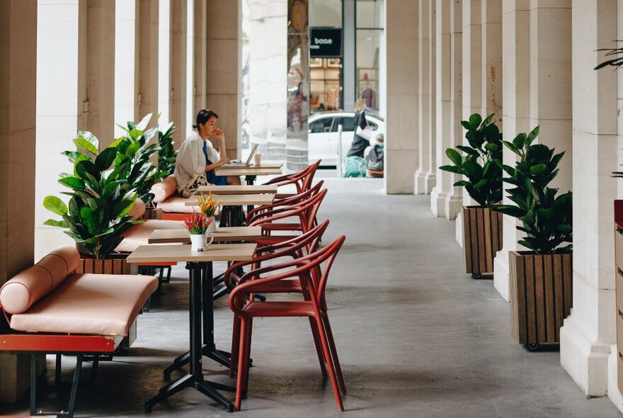 Archways of the Melbourne GPO Building, with bench seating and bentwood chairs on the concrete paved floor and plants in wooden planters/