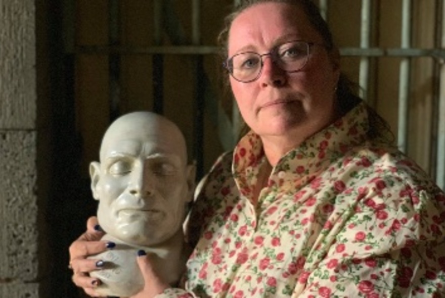 Author Deb Robinson holding a plaster death mask in her hands and staring directly ahead.