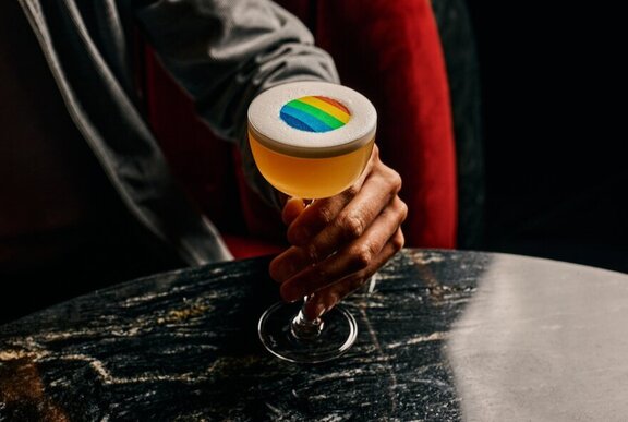 Hand holding a cocktail with a Pride multicolour design.