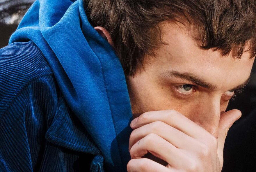 Close up of the face of music producer Big Ever, with his hand covering his mouth and only his eyes and the top of his nose visible, wearing a blue hoodie.