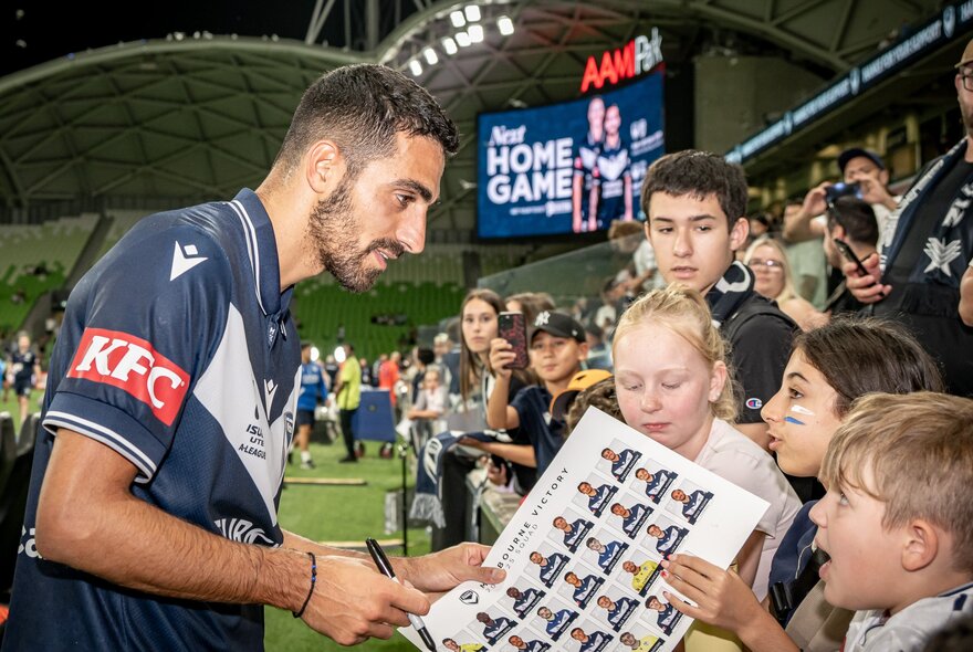 A Melbourne Victory soccer player interacts with young fans at a match. 