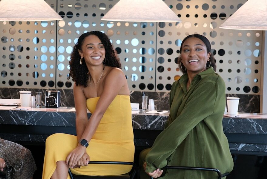 Two women in a bar setting smiling at something to their left. 